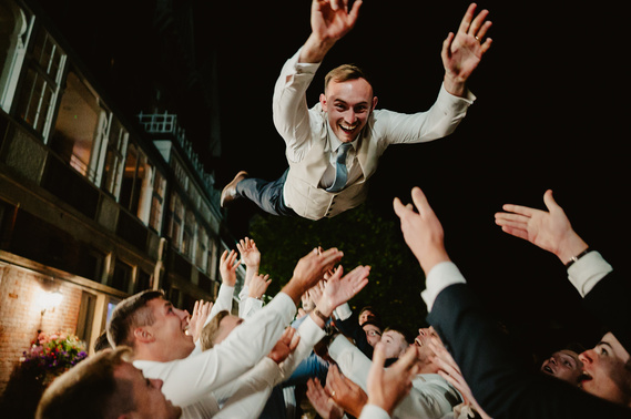 groom being thrown into the air during candid chaos during outdoor wedding reception at night
