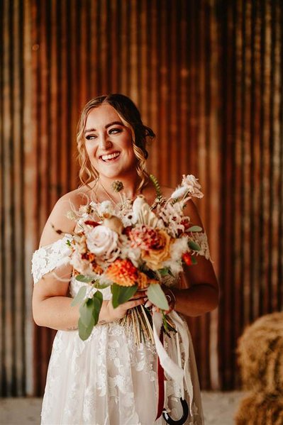 bride smiling holding dried flowers in front of rustic iron barn