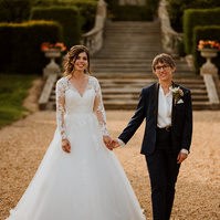 wedding couple smile to the camera whilst holding hands walking through the grounds during golden hour with the kent venue eastwell manor in the background