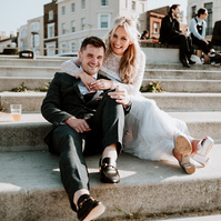 groom leaning back into the brides dress, her arms warpped around his shoulders whilst they both sit on margate steps which lead into the sea
