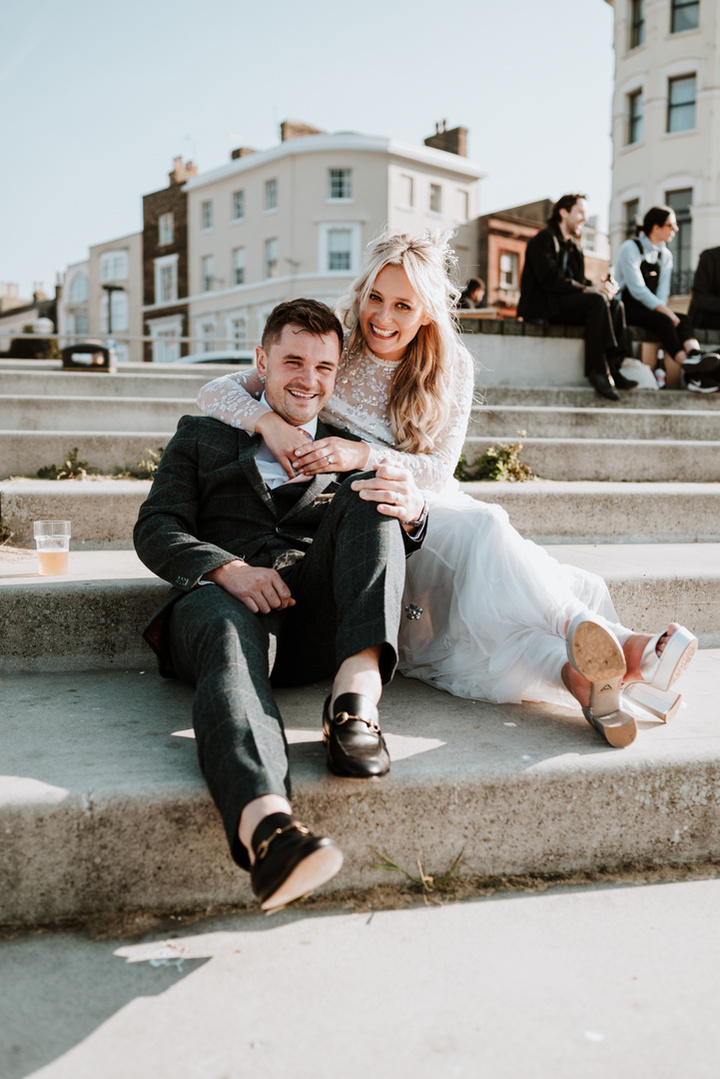 groom leaning back into the brides dress, her arms warpped around his shoulders whilst they both sit on margate steps which lead into the sea