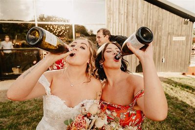 bride and her bridesmaid covered in champagne and both drinking champagne straight out of the bottle at silchester farm