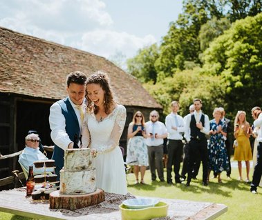 Kent wedding photographer takes portraits of couple cutting cake outdoors in the glorious sunshine at the amazing Kent wedding venue papermill
