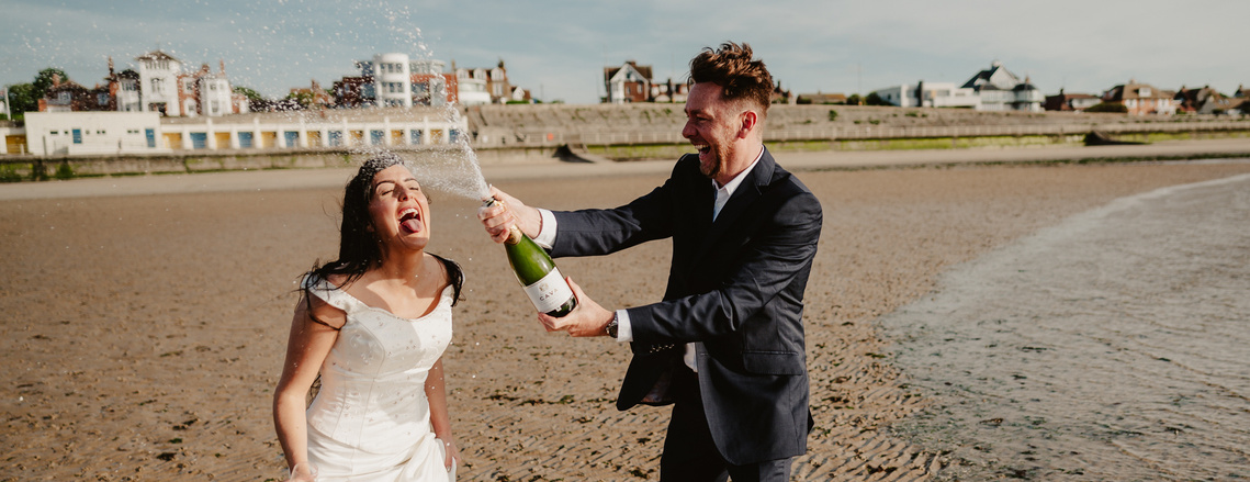 bride and groom spraying champagne during wedding portrait photography session on westgate beach in kent