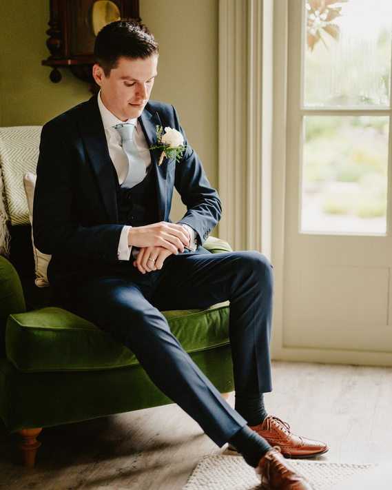 Groom in a blue suit posing on a chair at chapel house estate in thanet on his summer wedding day