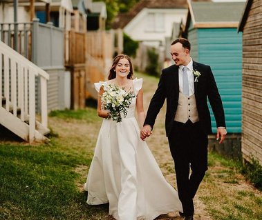 happy couple walking past beach huts on the whitstable coast in kent