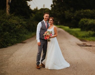 A couple a bride and groom posing in the middle of a countryside Road in the centre of a frame for a beautiful summer portrait in Kent outside their wedding venue