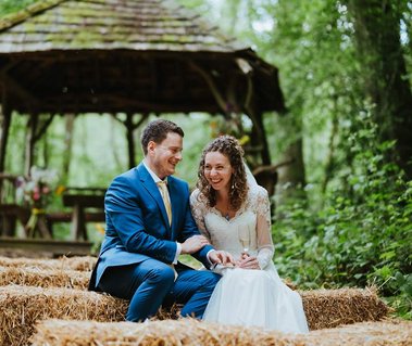 Bride and groom laughing candidly for a photograph sitting on a bale of hay at Kent woodland weddings