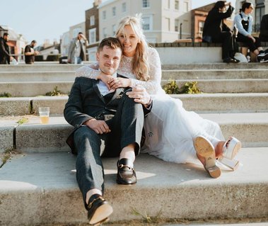Bride and groom laughing and smiling whilst drinking on the steps in Margate for their unique wedding outside the best wedding venue in kent