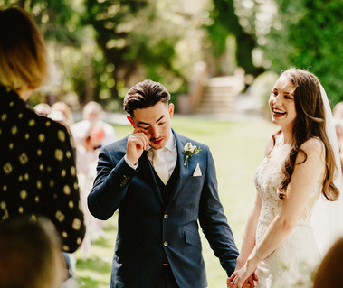 sussex Groom wipes away tears while his bride looks upon him lovingly and laughing