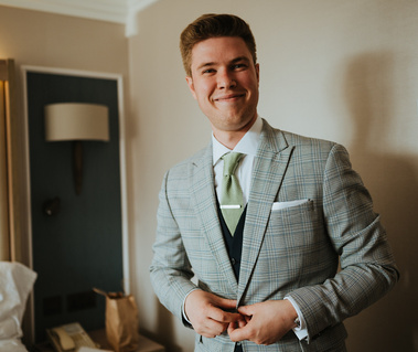 groom in a london hotel room smiling at camera in a check suit before wedding