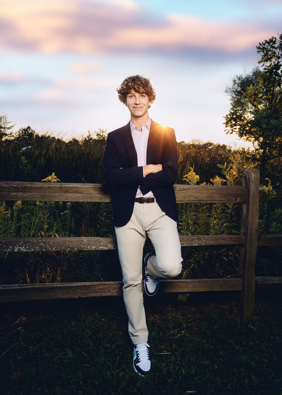 Senior portrait of a young man in a natural setting in Milwaukee, Wisconsin. This outdoor shot highlights his unique style and individuality, framed by lush greenery and autumn foliage. 