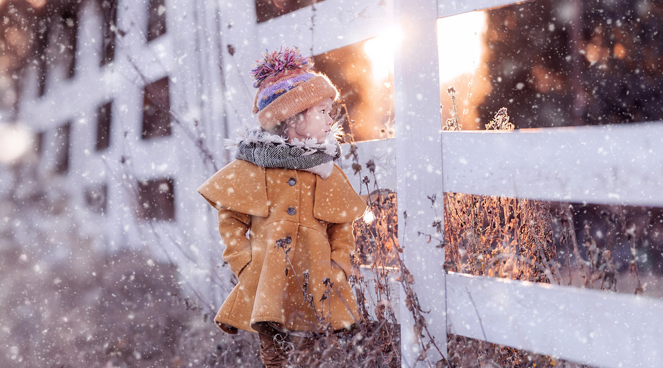 Captivating child portrait in Cedarburg Wisconsin during the snow fall in November. Beautiful sunset behind the fence and warm golden light and color tone. 
