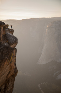 A person stands on the edge of Taft Point with their arms in the air.