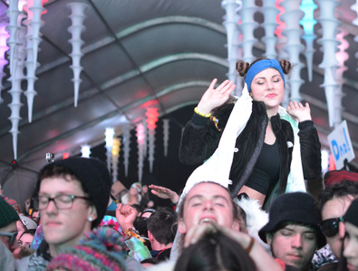 A girl is dancing while sitting on her friend's shoulders in the crowd.
