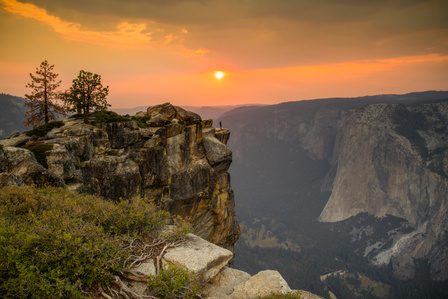 A person stands on the edge of Taft Point in Yosemite while the sun sets behind them.