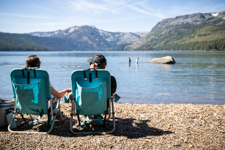 A couple lounges on the beach at Fallen Leaf Lake while their kids play in the water.