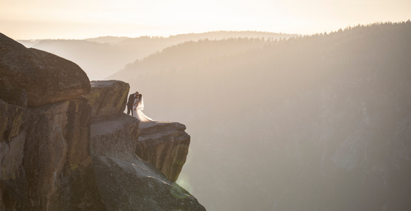 A groom dips his bride on Taft Point overlooking Yosemite Valley during the sunset.