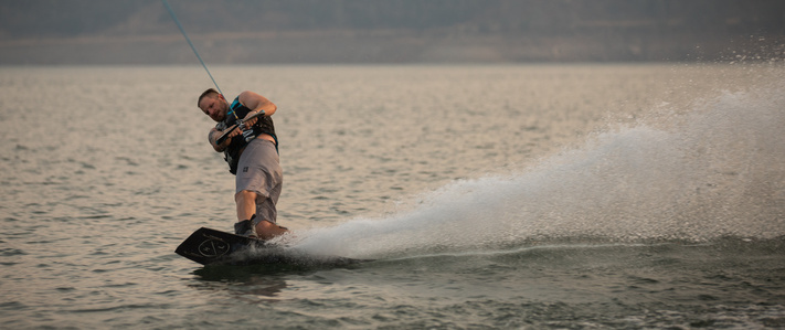 Man wakeboarding on calm water during sunset.