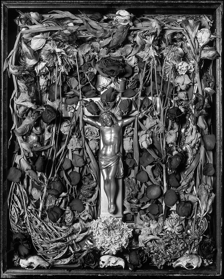 Still life of various objects arranged around a framed crucifixion.