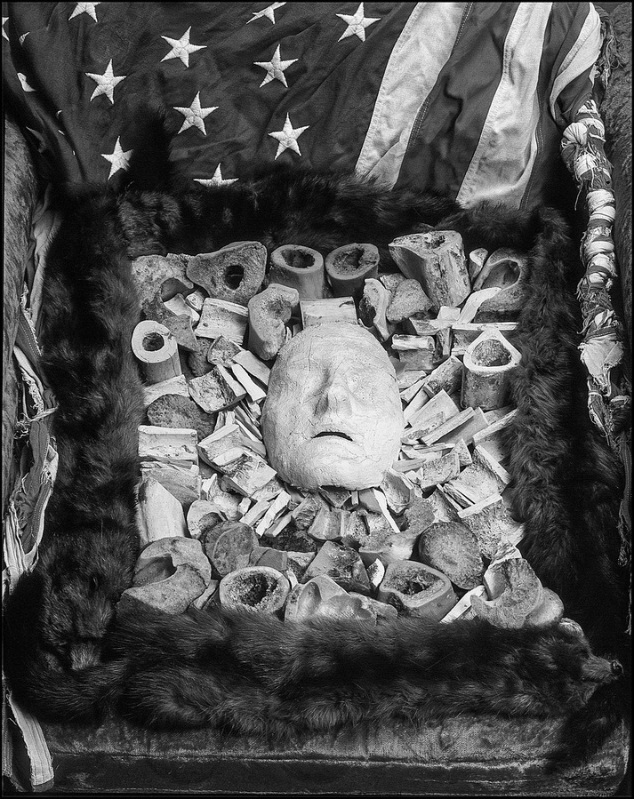 Still life of a life mask with beef bones, furs, and a US flag.