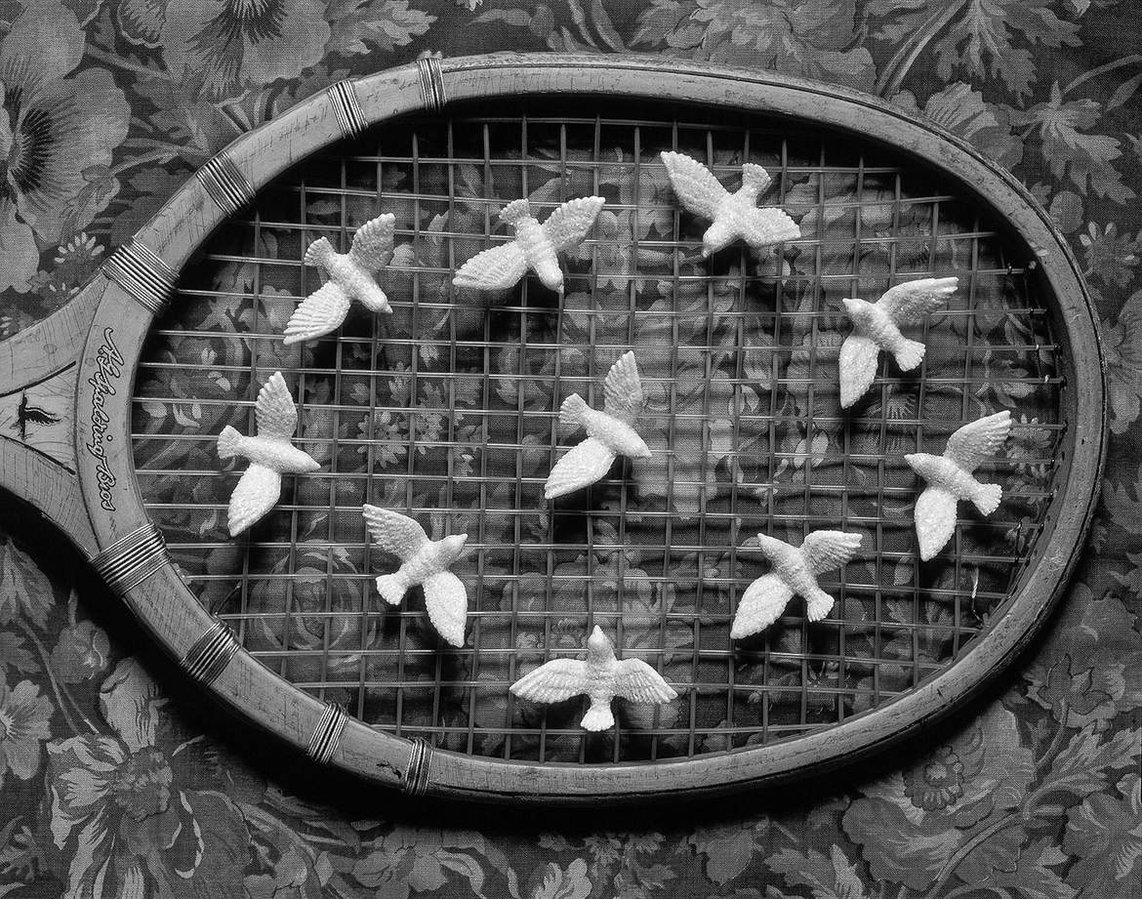 Still life of toy plastic doves arranged on an old wooden tennis racquet.