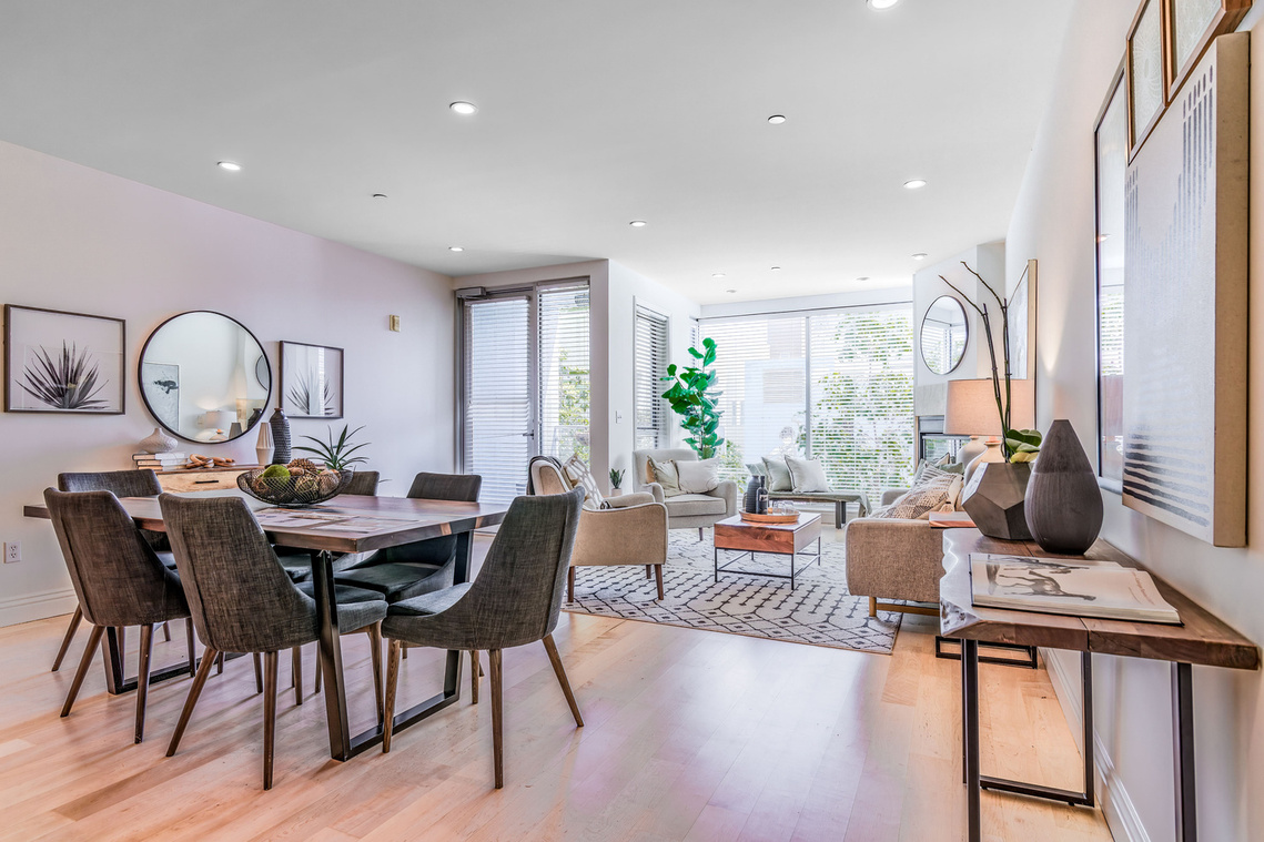 Interior entrance to the well-staged open-concept dining area and living room with a far wall of full-length windows and a door to a small deck.