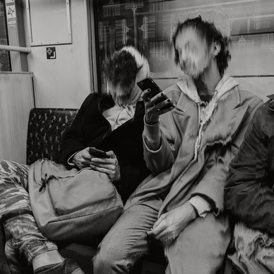 Two teenagers sitting on subway, not engaging with each other while scrolling on their phones.
