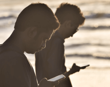 Two men looking down and staring at phone screens instead of looking up at the ocean view.