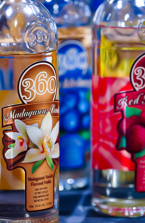 Three bottles of 360 vodka in 3 flavors, blueberry, raspberry, and vanilla. Brightly colored tables.