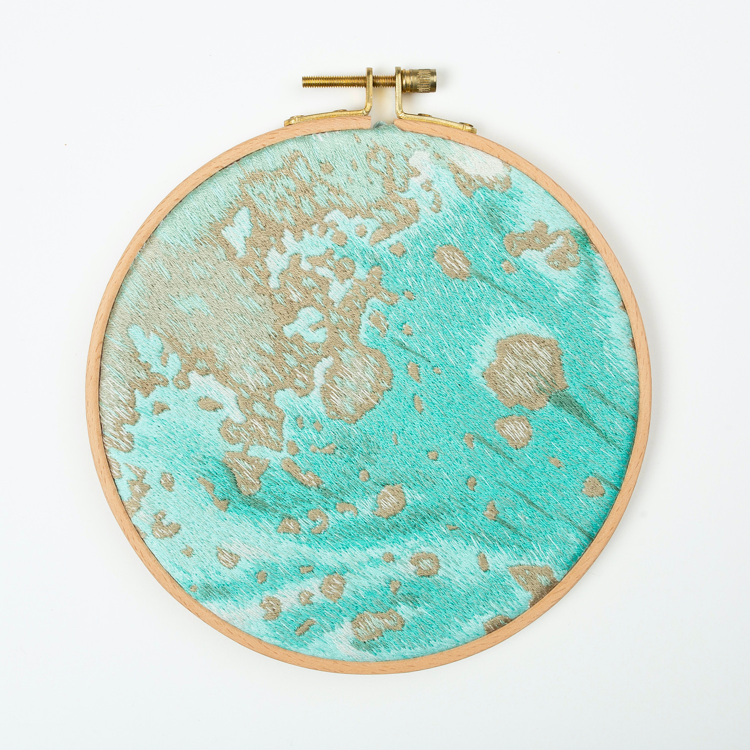 A hand embroidered art piece framed in a round, wooden embroidery hoop. The vibrant colours of the piece depict a satellite view of the ocean.