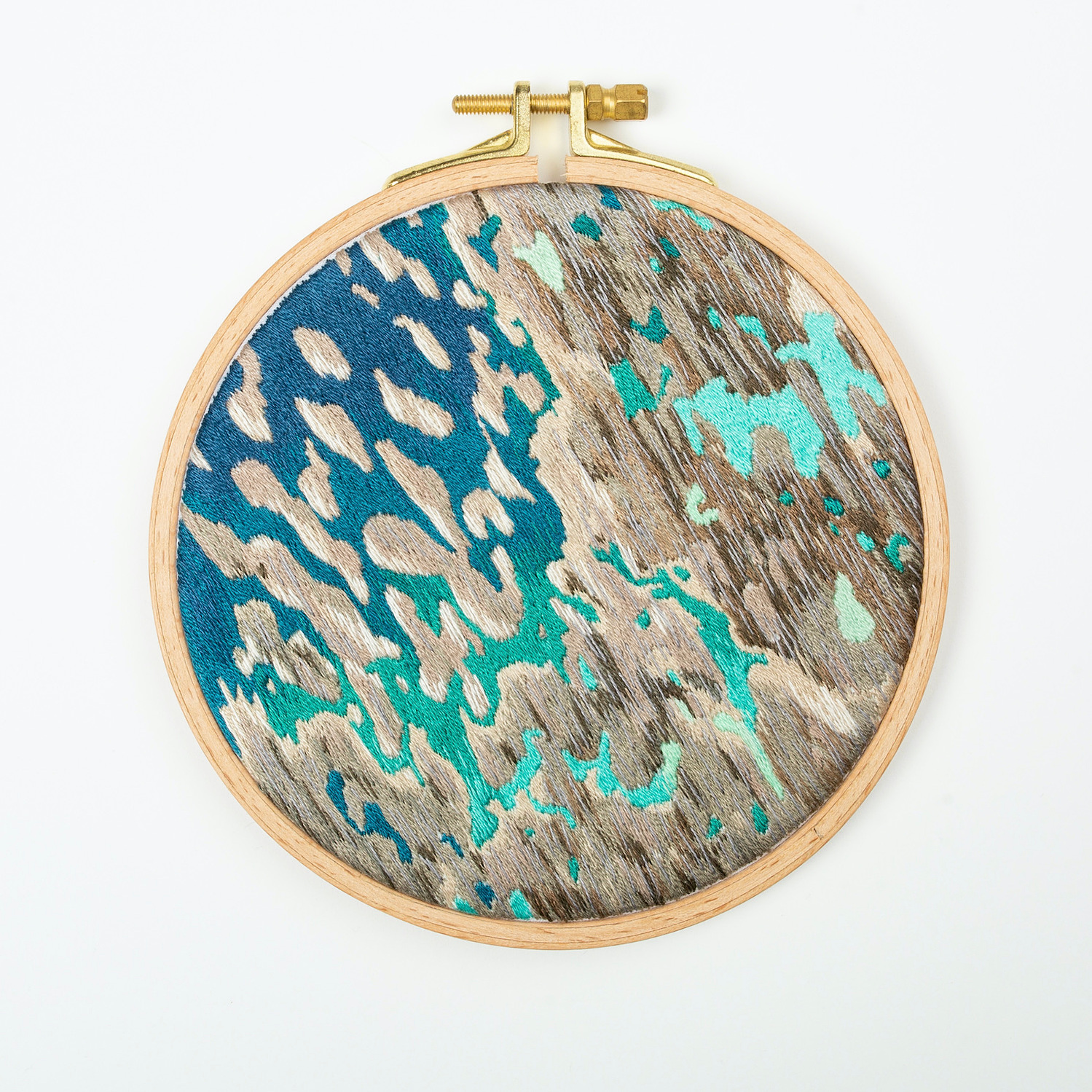 A hand embroidered art piece framed in a round, wooden embroidery hoop. The vibrant colours of the piece depict a satellite view of the ocean.