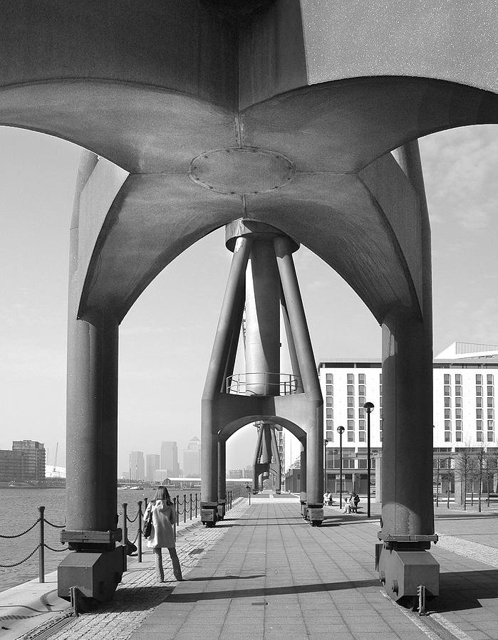 A black and white photo of a Dockland Crane and woman by Mark Burley