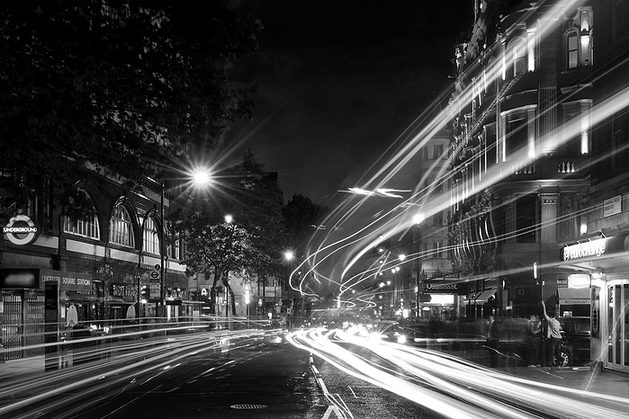 A black and white photo of Big Ben and light tails on the bridge at night by Mark Burley