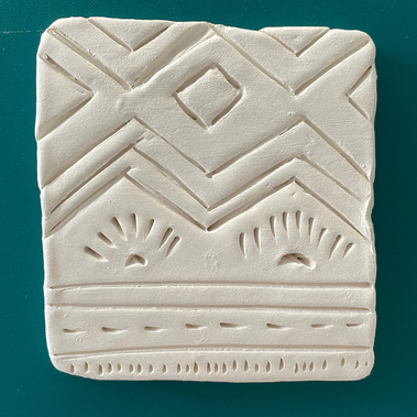 A solitary tile carved with an abstract geometric pattern, with squares and triangles and a setting sun motif, and some lines at the bottom. This is carved into the tile so that one could feel it if they touched it. 