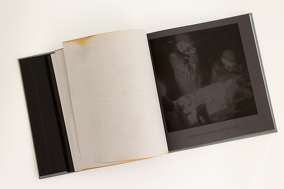 A spread in the book. The left hand page is light grey paper with burnt, scorch marks around the edges. The right hand page is black paper with a black, half tone photograph of people working in the damaged power plant.