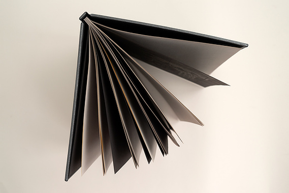 A top-down view of the book showing the tops of the pages. They are made of a mixture of black and grey paper, with brown scorch marks.