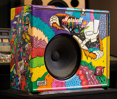 A Marshall guitar amplifier painted by hand with bright, multicoloured stripes and kooky cartoon characters. The fretcloth has been removed to expose the black speaker.