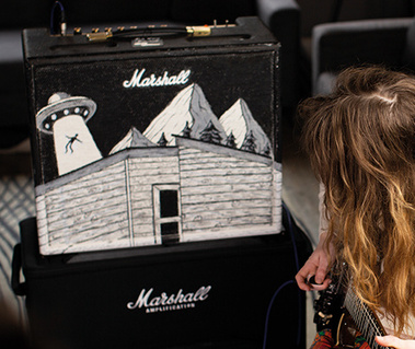 A Marshall amplifier painted by hand entirely in black and white. The front of the amplifier shows a cabin in the mountains and a silhouette of a person being beamed up into a UFO.