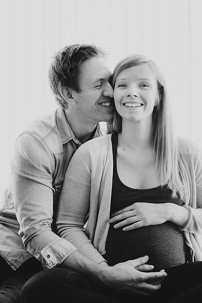 Mann holder rundt en gravid kvinne og smiler