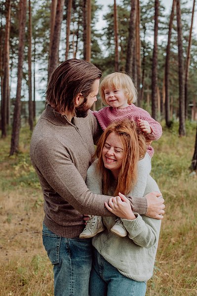 Kvinne bærer barnet sitt på skuldrene mens de står inntil far og ler