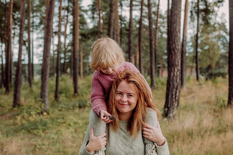 Kvinne holder barnet sitt på skuldrene i en luftig skog