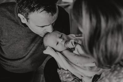 Kvinne holder nyfødt baby og mann kysser babyen på hodet