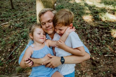 Far holder rundt og gir en klem til to barn en varm sommerdag