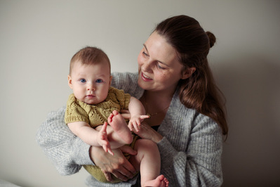 Kvinne holder en baby i armene foran en beige vegg