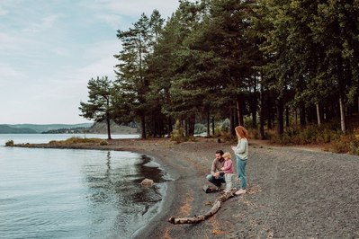 Familie på tre står ved vannkanten og kaster stein i vannet