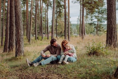 Familie på tre sitter på bakken i en furuskog