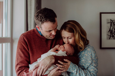 Mor og far holder nyfødt baby mens moren kysser babyen på hodet