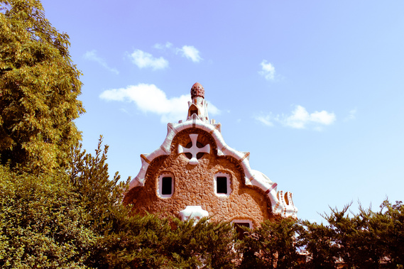 Landscape oriented vintage looking color photo of the unique style architecture brown building with curvy white capped roof and abstract designs by Antoni Gaudi at Park Guell in Barcelona 