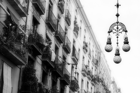Black and White photo of an Intricate street lantern lamp in Barcelona Spain set against classic Spanish architecture balconies with flower pots
